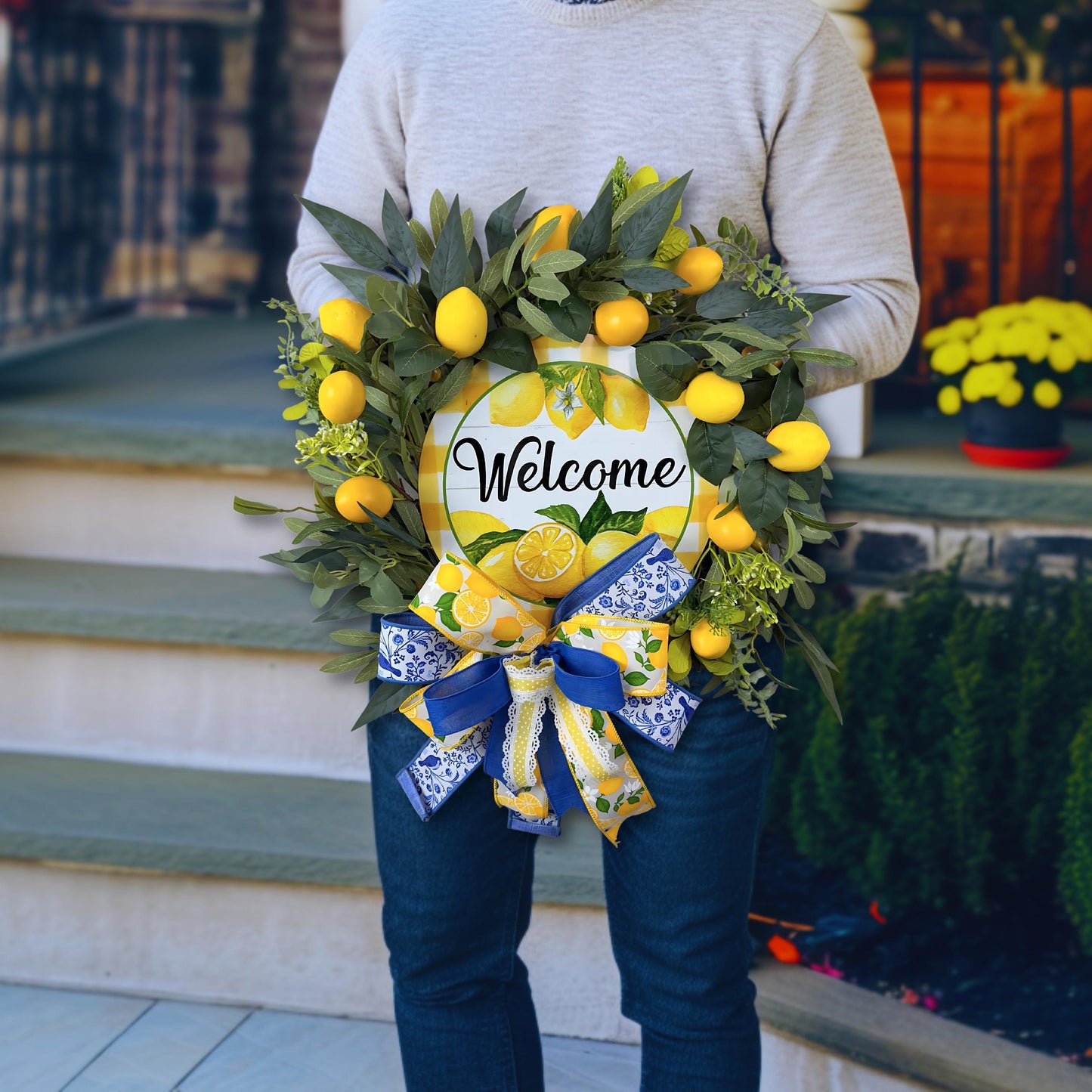 Person holding lemon welcome wreath to show size and fullness, featuring realistic lemons, greenery, and decorative bow