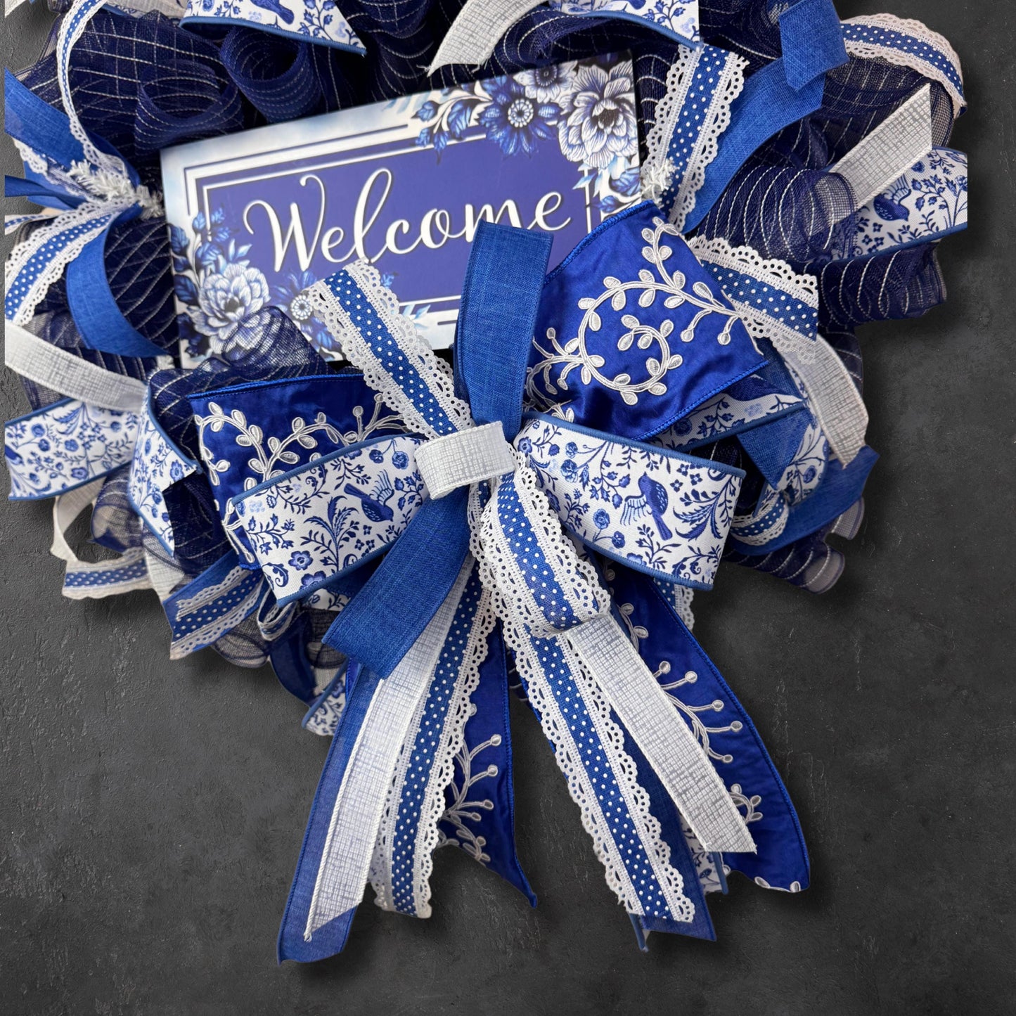 Detailed shot of luxury blue and white ribbons with lace trim on a chinoiserie-style mesh wreath for front door or home decor.