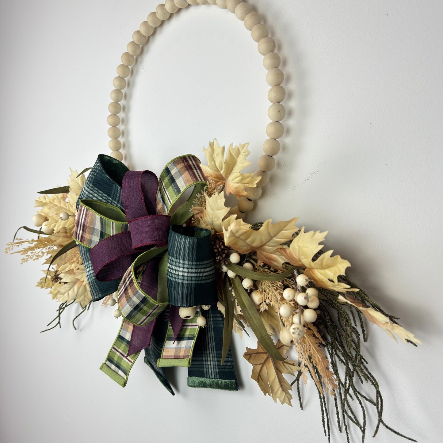 Detail view of the natural wood beaded hoop base with floral accents and autumn greenery attached.