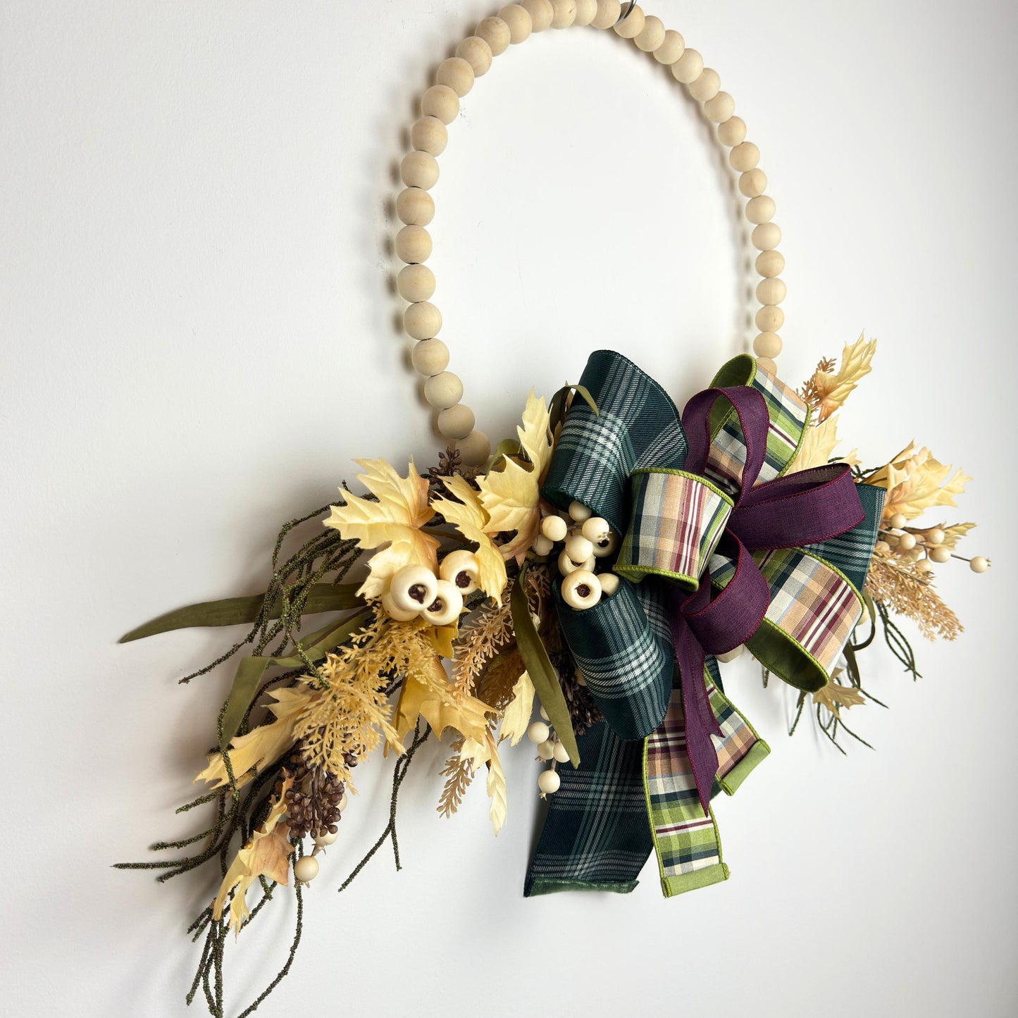 Close-up of burgundy and green plaid bow on a beaded hoop wreath with golden maple leaves and cream berries.