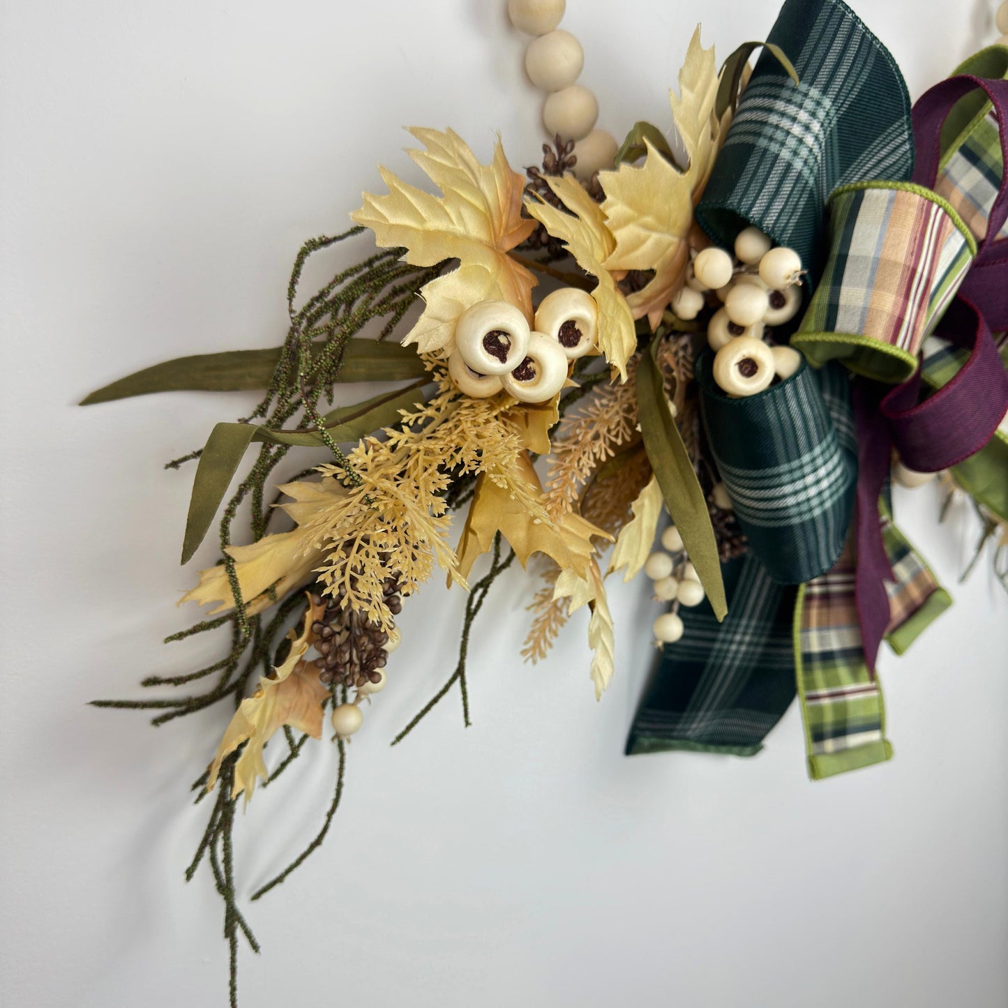 Close-up of artificial maple leaves and cream berries on fall wreath, highlighting intricate seasonal detailing.