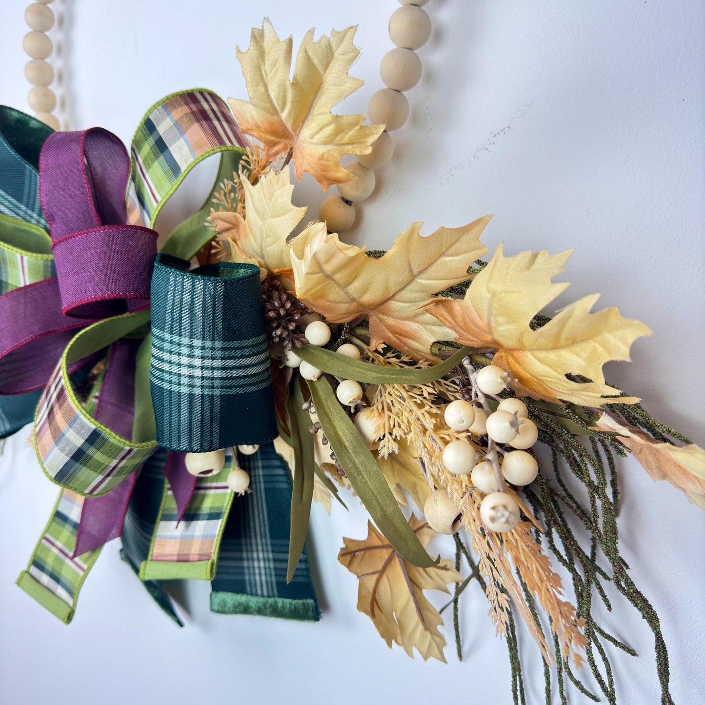 Close-up of layered wired ribbon bow featuring plaid and solid burgundy tones on a fall-themed wreath.