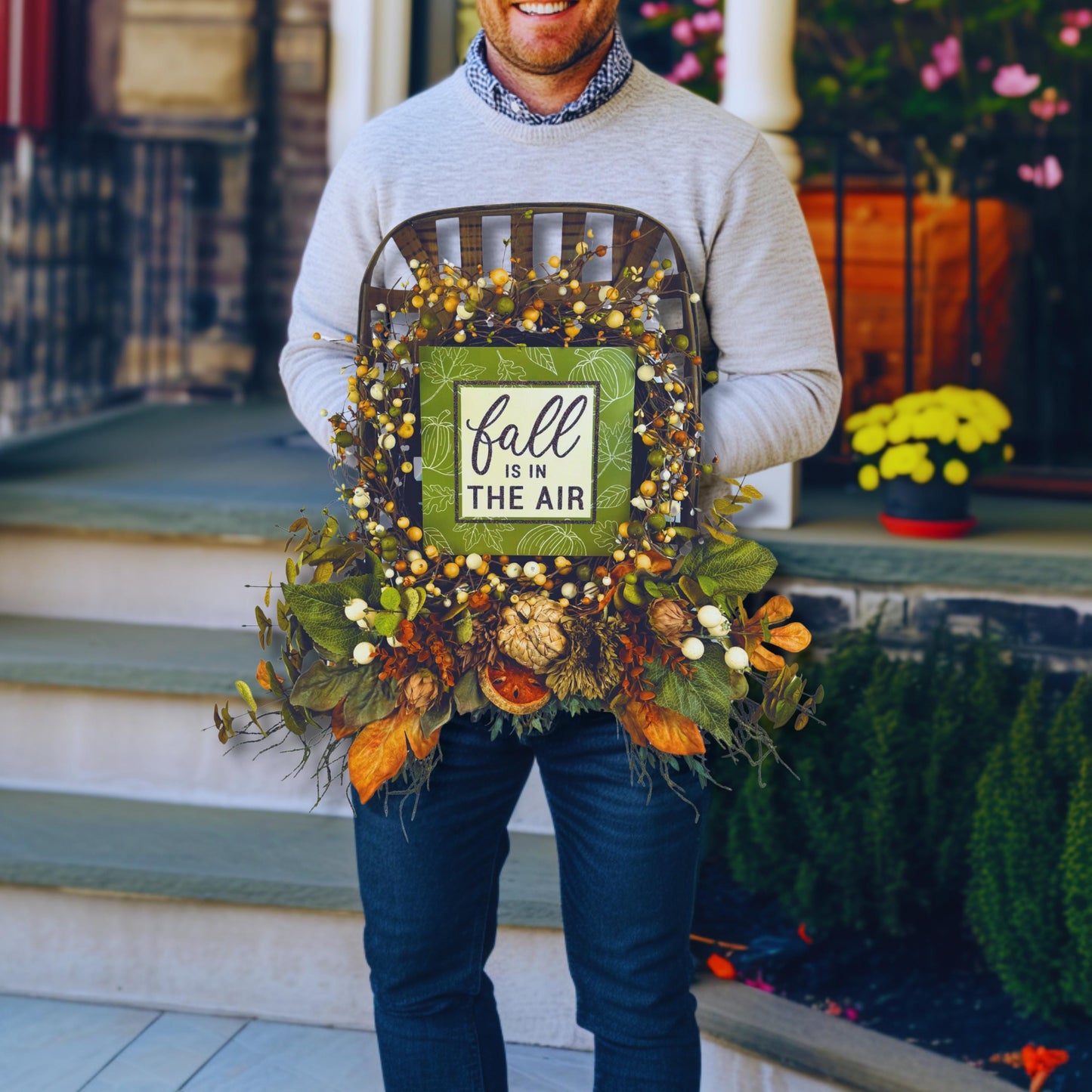 Large fall wreath for porch décor held by smiling man, showing scale and rustic design