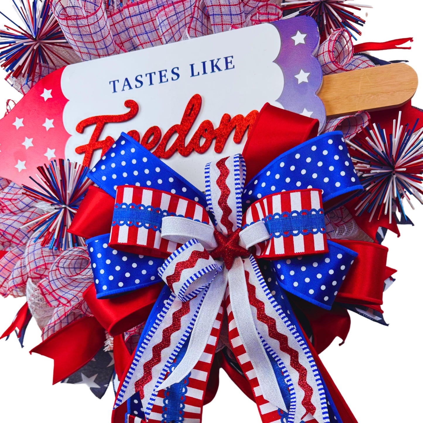 Close-up detail of patriotic bow on handmade 4th of July wreath, featuring red glitter star, polka dot and striped ribbons for festive summer decor
