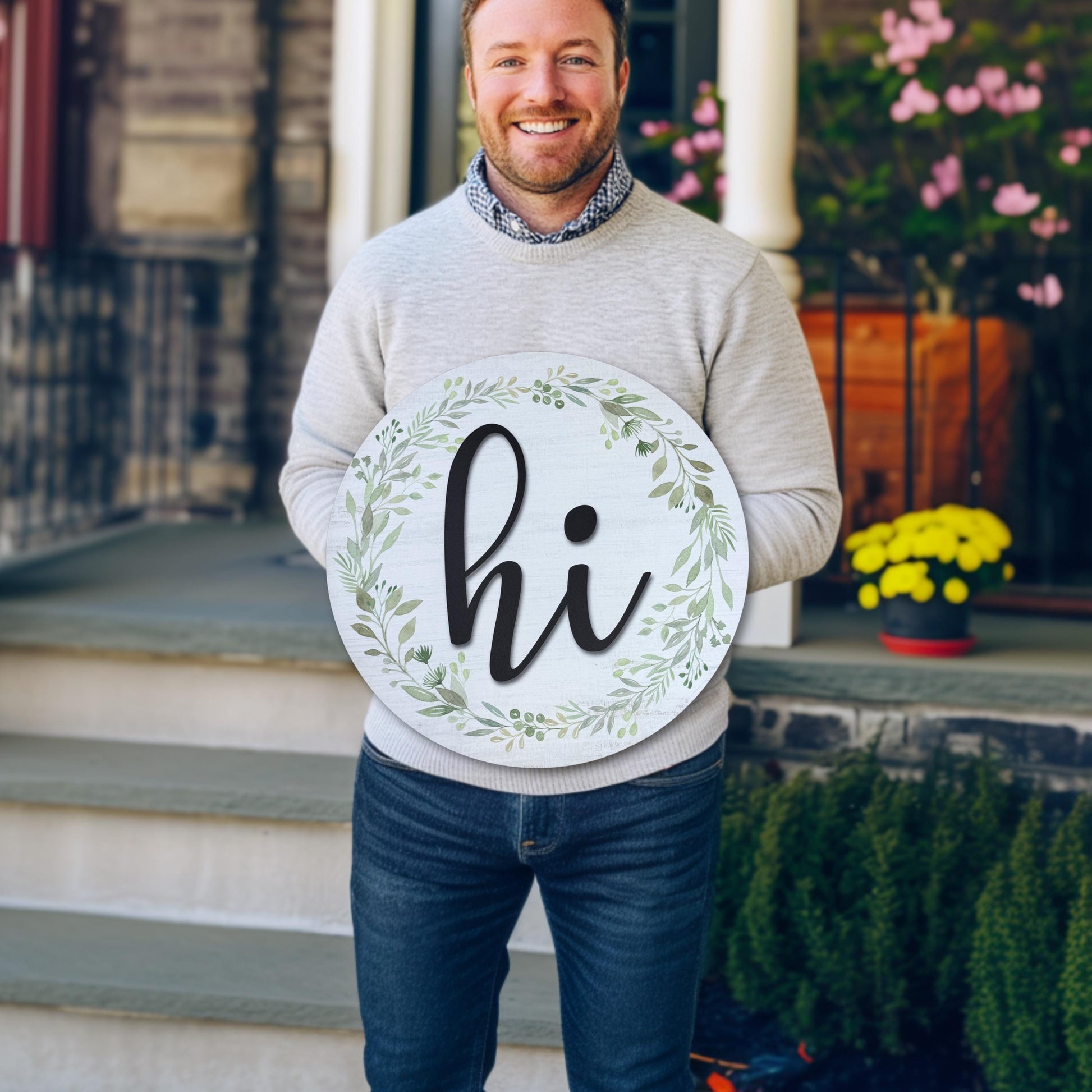 Man holding 18-inch round wooden hi door sign with greenery wreath on front porch, perfect size demonstration for entryway decor