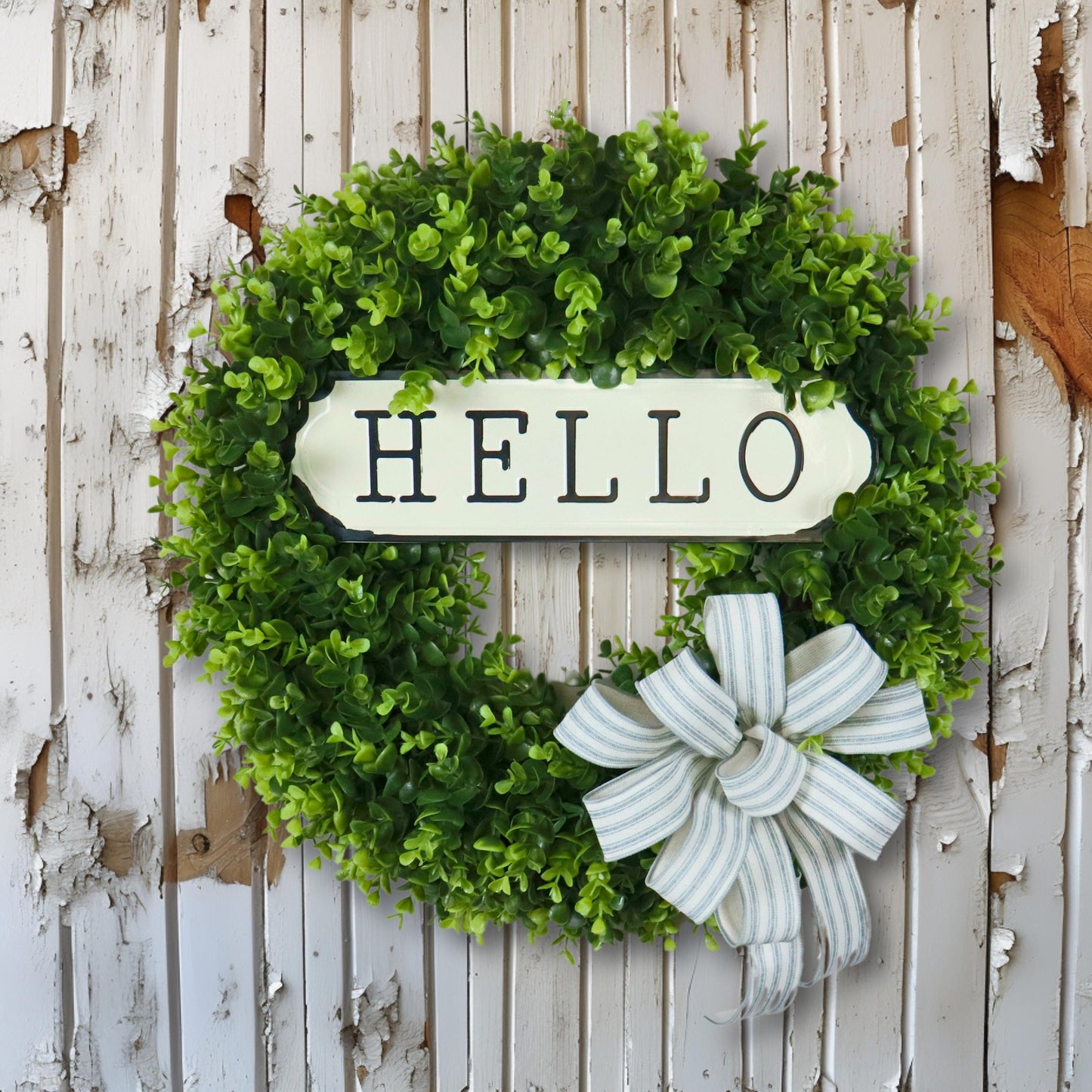 Farmhouse boxwood wreath with metal hello sign and striped bow, rustic front door decor, artificial greenery wreath for home entryway.