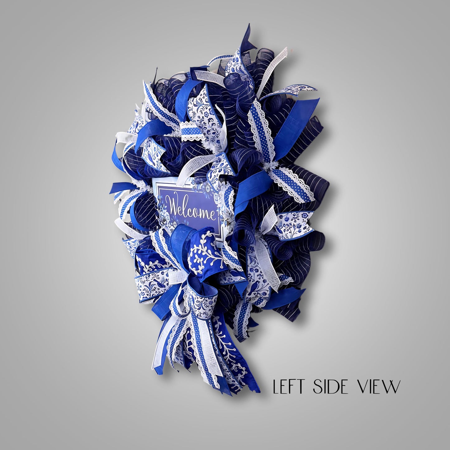 Left side view of lush blue and white welcome wreath, highlighting mesh layers and premium ribbon design for elegant entryway styling.