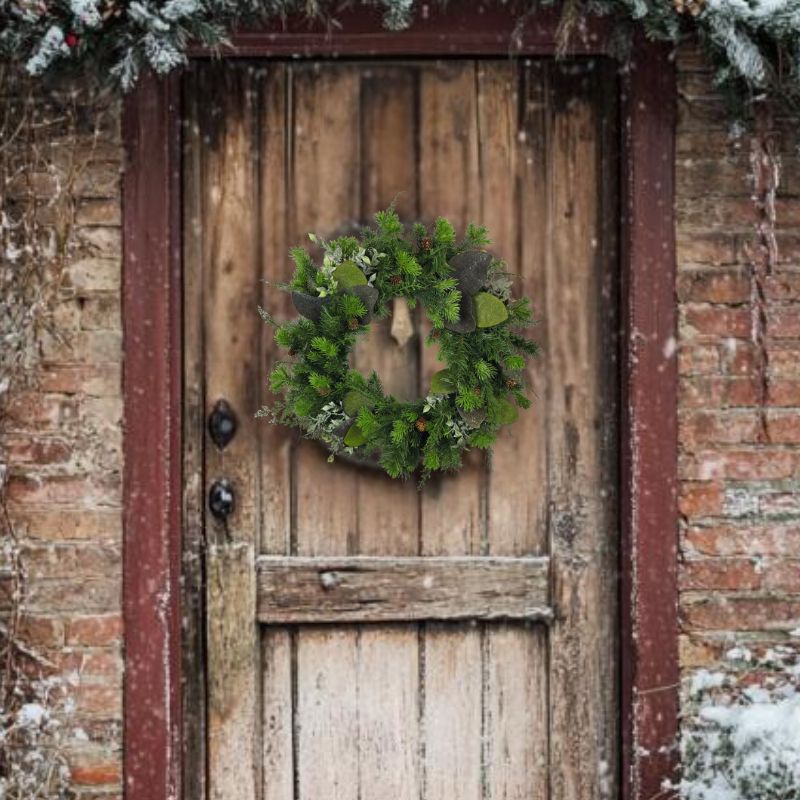 Rustic winter wreath on a weathered door with lifelike evergreen and pinecones, perfect for outdoor or indoor winter decor.